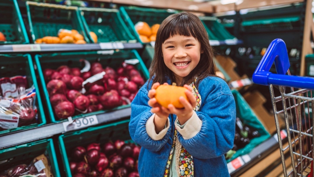 school-aged girl holding an orange in a supermarket